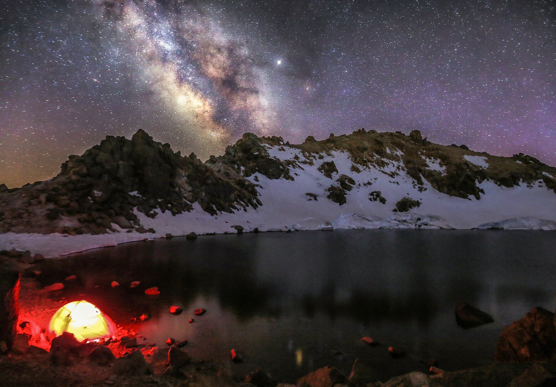 The Milky Way above Sabalan's snowy crater lake, with a glowing tent on the shore